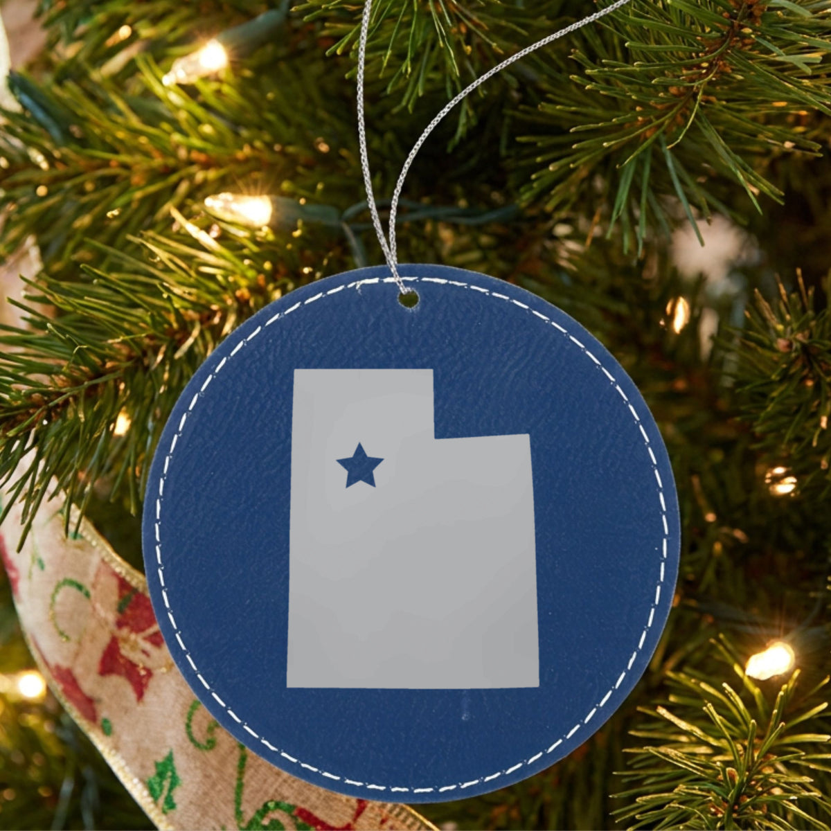 Blue leatherette round Christmas ornament laser engraved with the Utah Star Accent design, hanging on a tree