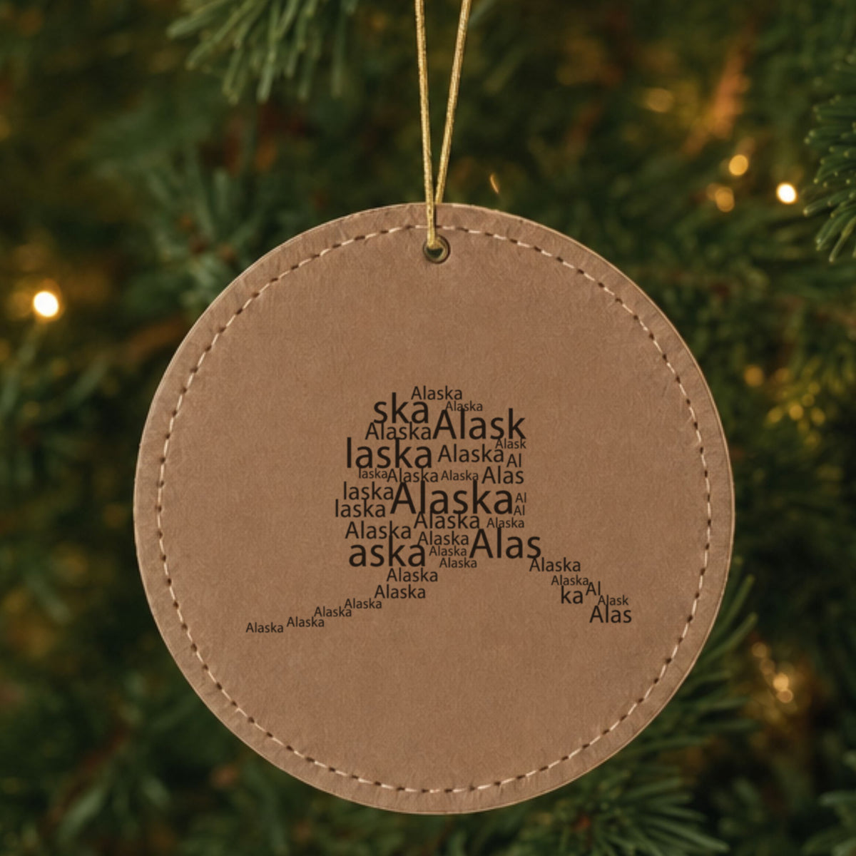 Brown leatherette round Christmas ornament laser engraved with the Alaska Word Cloud design, hanging on a tree