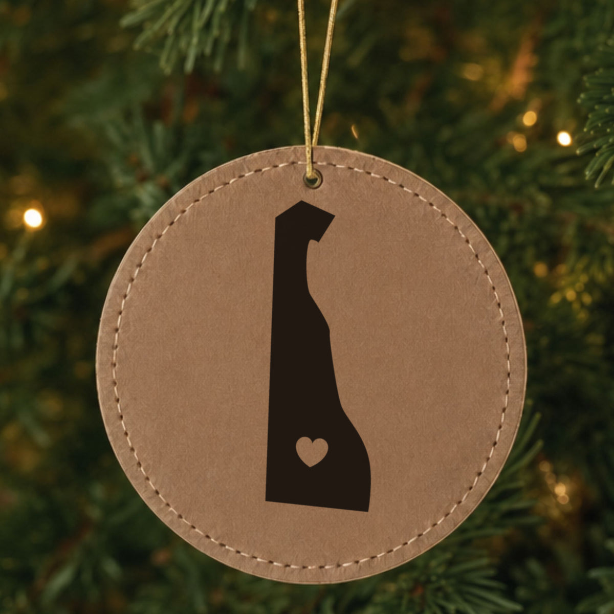 Brown leatherette round Christmas ornament laser engraved with the Delaware Heart Accent design, hanging on a tree