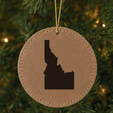 Brown leatherette round Christmas ornament laser engraved with the Idaho Engraved State design, hanging on a tree