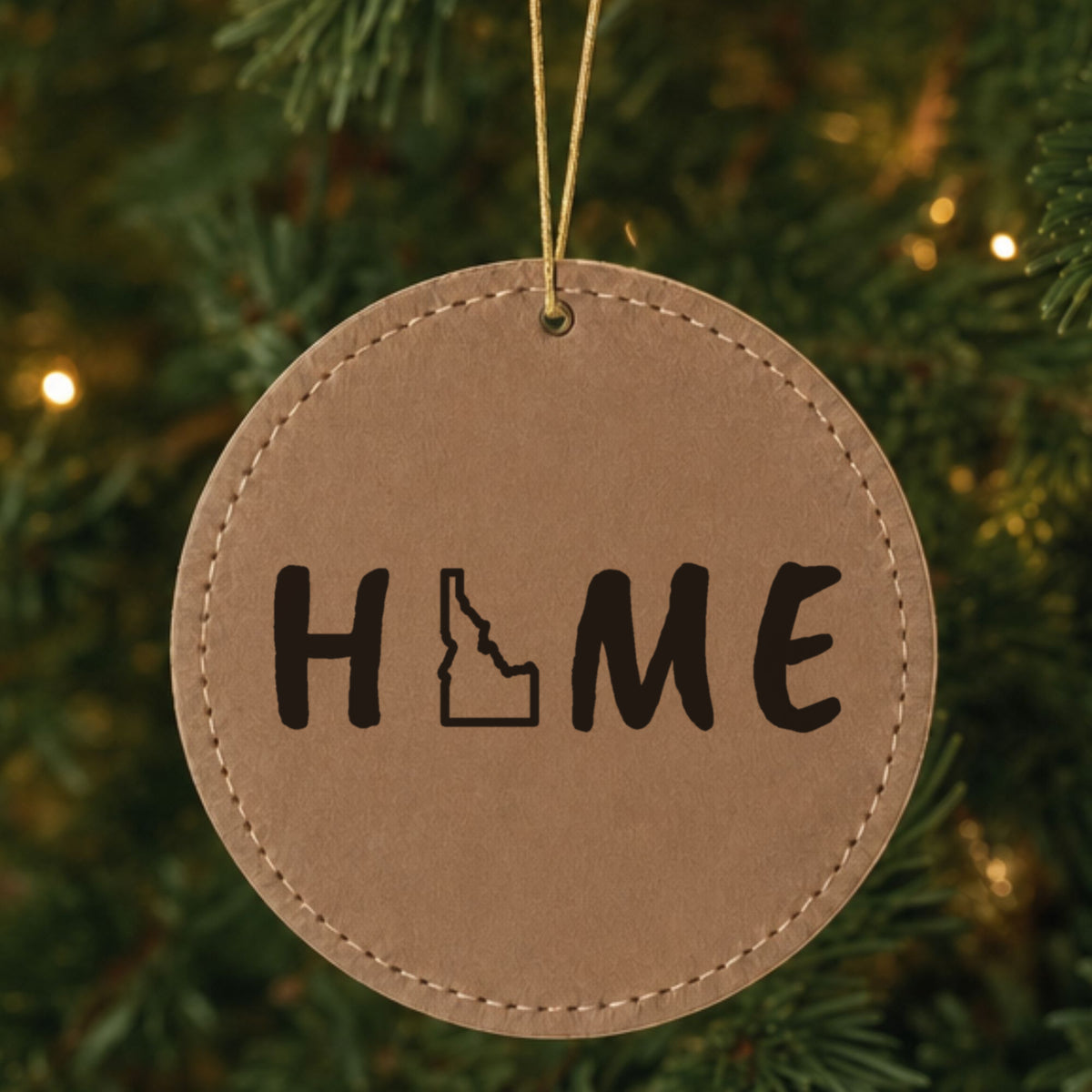 Brown leatherette round Christmas ornament laser engraved with the Idaho HOME Outline design, hanging on a tree