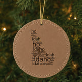 Brown leatherette round Christmas ornament laser engraved with the Idaho Word Cloud design, hanging on a tree