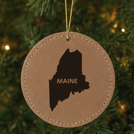 Brown leatherette round Christmas ornament laser engraved with the Maine Bold State Name design, hanging on a tree