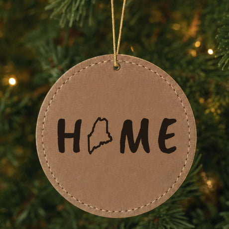 Brown leatherette round Christmas ornament laser engraved with the Maine HOME Outline design, hanging on a tree