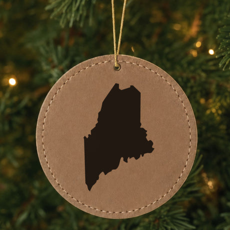 Brown leatherette round Christmas ornament laser engraved with the Maine Engraved State design, hanging on a tree
