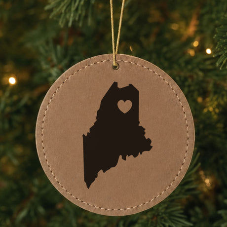 Brown leatherette round Christmas ornament laser engraved with the Maine Heart Accent design, hanging on a tree