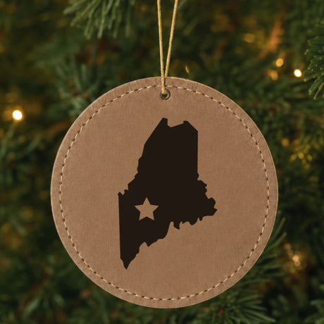 Brown leatherette round Christmas ornament laser engraved with the Maine Star Accent design, hanging on a tree