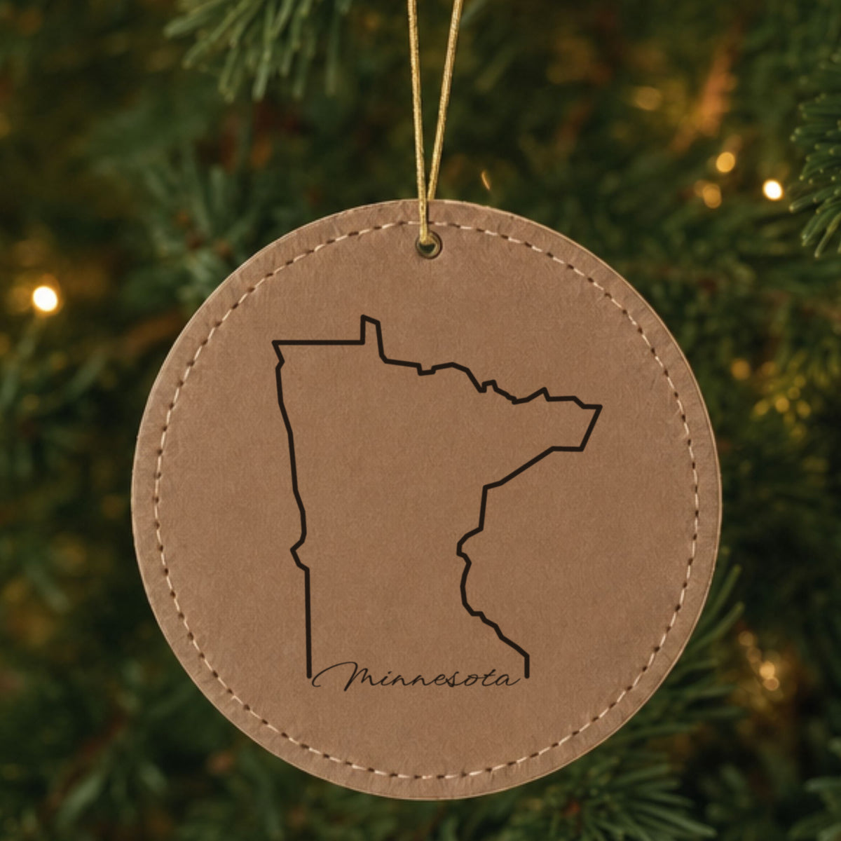 Brown leatherette round Christmas ornament laser engraved with the Minnesota Minnesota Script design, hanging on a tree