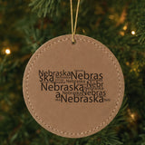 Brown leatherette round Christmas ornament laser engraved with the Nebraska Word Cloud design, hanging on a tree