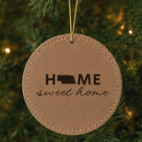 Brown leatherette round Christmas ornament laser engraved with the Nebraska Home Sweet Home design, hanging on a tree