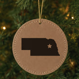 Brown leatherette round Christmas ornament laser engraved with the Nebraska Star Accent design, hanging on a tree