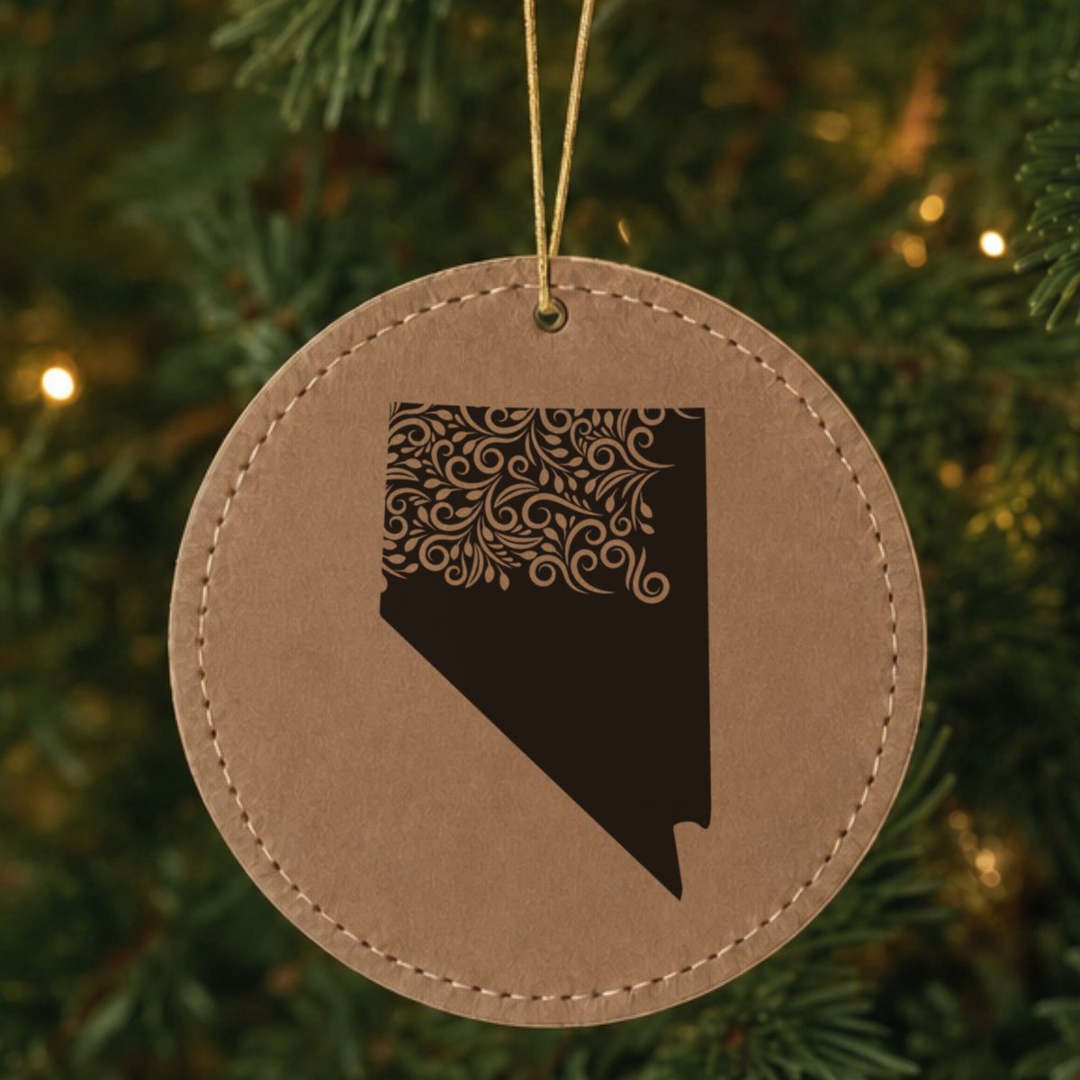 Brown leatherette round Christmas ornament laser engraved with the Nevada Floral Damask design, hanging on a tree