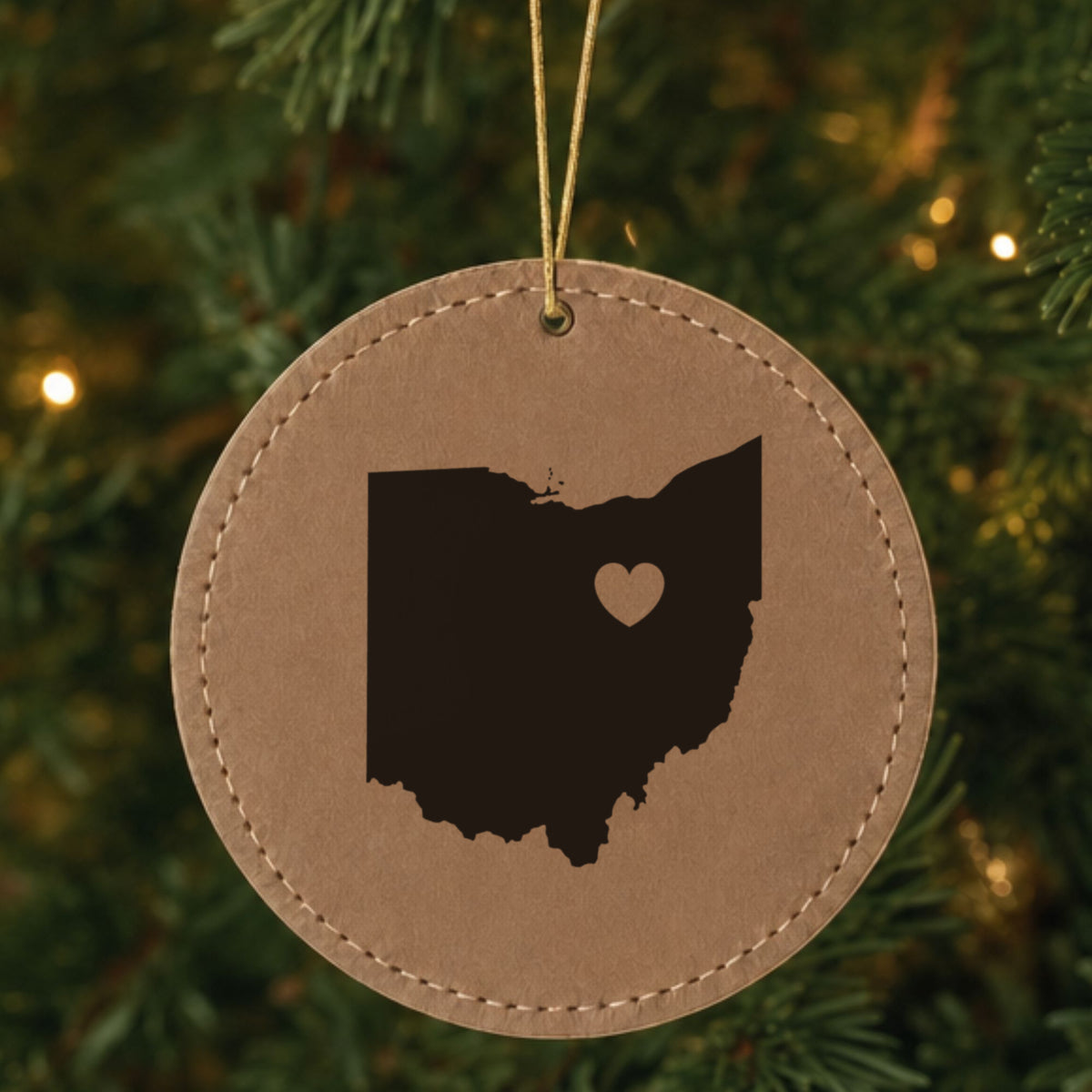 Brown leatherette round Christmas ornament laser engraved with the Ohio Heart Accent design, hanging on a tree