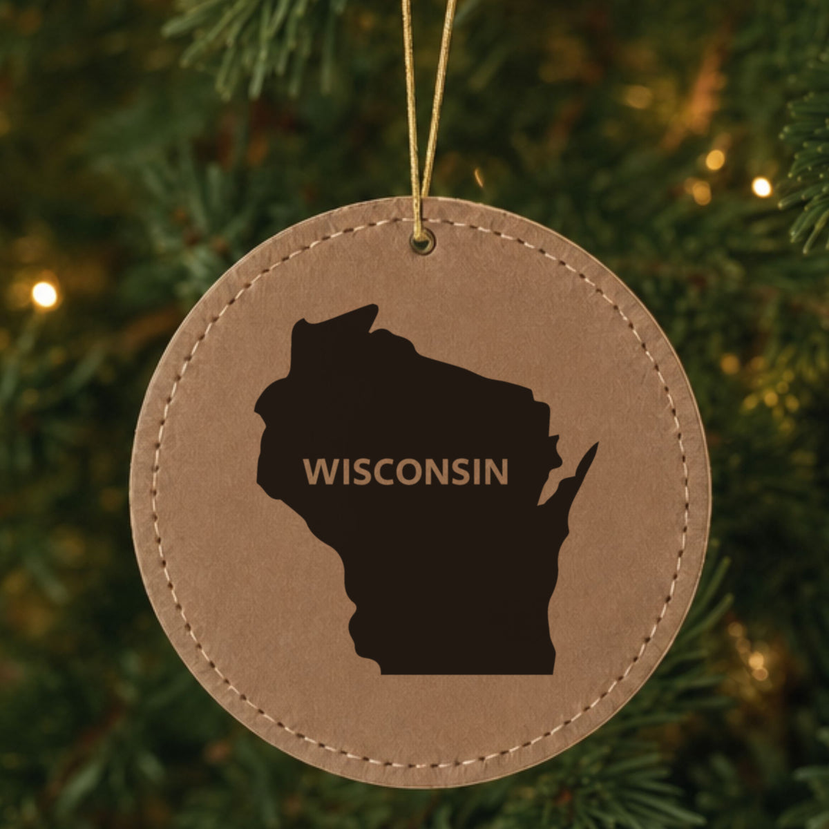 Brown leatherette round Christmas ornament laser engraved with the Wisconsin Bold State Name design, hanging on a tree