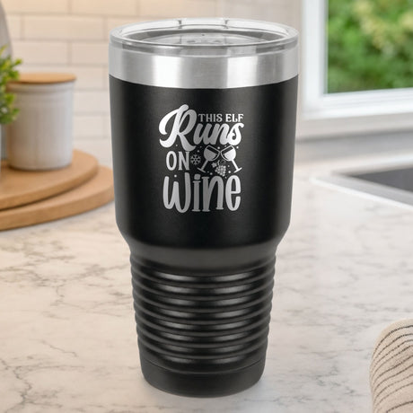 Black 30 oz tumbler laser engraved with "This Elf Runs on Wine", on a kitchen counter