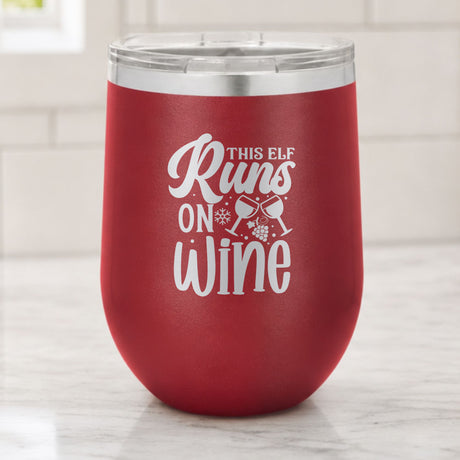 Maroon 12 oz stemless wine tumbler laser engraved with "This Elf Runs on Wine", on a kitchen counter