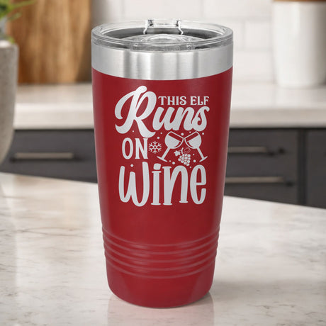 Maroon 20 oz tumbler laser engraved with "This Elf Runs on Wine", on a kitchen counter