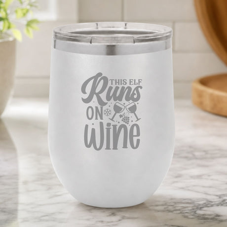 White 12 oz stemless wine tumbler laser engraved with "This Elf Runs on Wine", on a kitchen counter