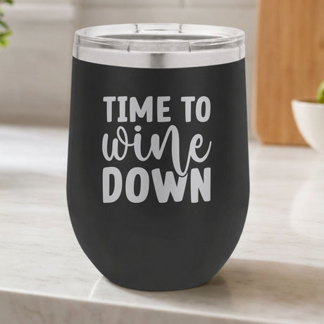 Black 12 oz stemless wine tumbler laser engraved with "Time to Wine Down", on a kitchen counter