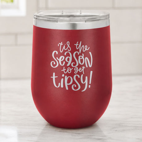 Maroon 12 oz stemless wine tumbler laser engraved with "'Tis the Season to Get Tipsy", on a kitchen counter