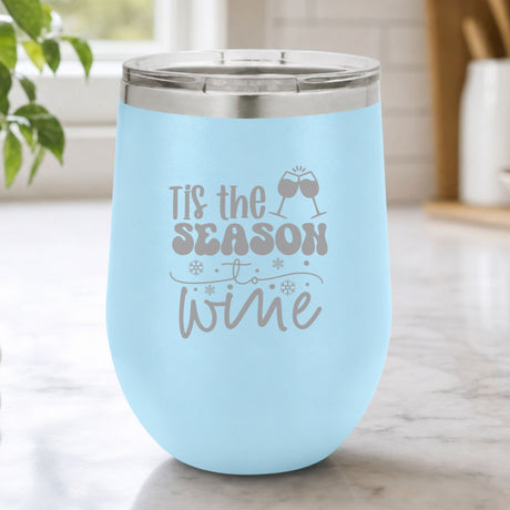 Light Blue 12 oz stemless wine tumbler laser engraved with "'Tis the Season to Wine", on a kitchen counter