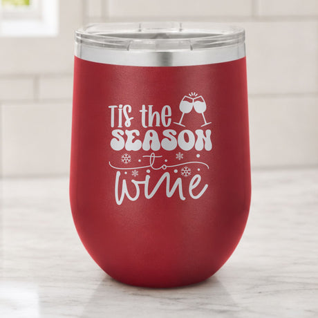 Maroon 12 oz stemless wine tumbler laser engraved with "'Tis the Season to Wine", on a kitchen counter
