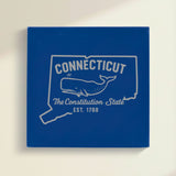 Close up of the Connecticut design engraved on Blue leatherette: a sperm whale, "The Constitution State", EST. 1788