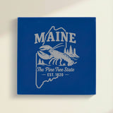 Close up of the Maine design engraved on Blue leatherette: a lobster, pines and a lighthouse, "The Pine Tree State", EST. 1820