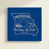 Close up of the Missouri design engraved on Blue leatherette: the Gateway Arch, a riverboat and a mule, "The Show-Me State", EST. 1821