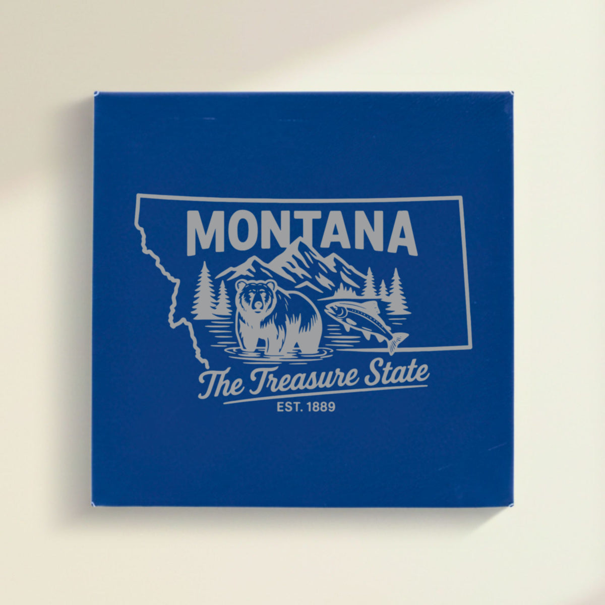 Close up of the Montana design engraved on Blue leatherette: a grizzly bear, a trout and mountain peaks, "The Treasure State", EST. 1889