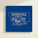 Close up of the Montana design engraved on Blue leatherette: a grizzly bear, a trout and mountain peaks, "The Treasure State", EST. 1889