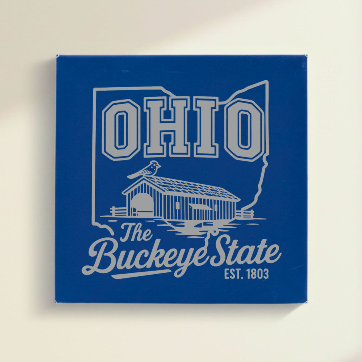 Close up of the Ohio design engraved on Blue leatherette: a covered bridge and a cardinal, "The Buckeye State", EST. 1803