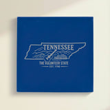 Close up of the Tennessee design engraved on Blue leatherette: a guitar, a riverboat and the Smoky Mountains, "The Volunteer State", EST. 1796