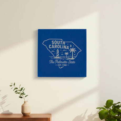 Blue leatherette wall sign engraved with a South Carolina design of a striped lighthouse, palm trees and a beach under a crescent moon, hanging on a wall