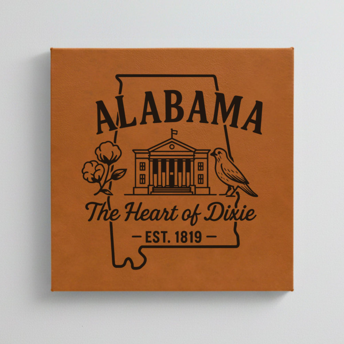 Close up of the Alabama design engraved on Brown leatherette: the capitol building, a cotton boll and a yellowhammer, "The Heart of Dixie", EST. 1819