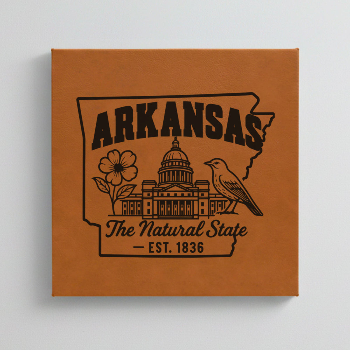 Close up of the Arkansas design engraved on Brown leatherette: the capitol dome, an apple blossom and a mockingbird, "The Natural State", EST. 1836