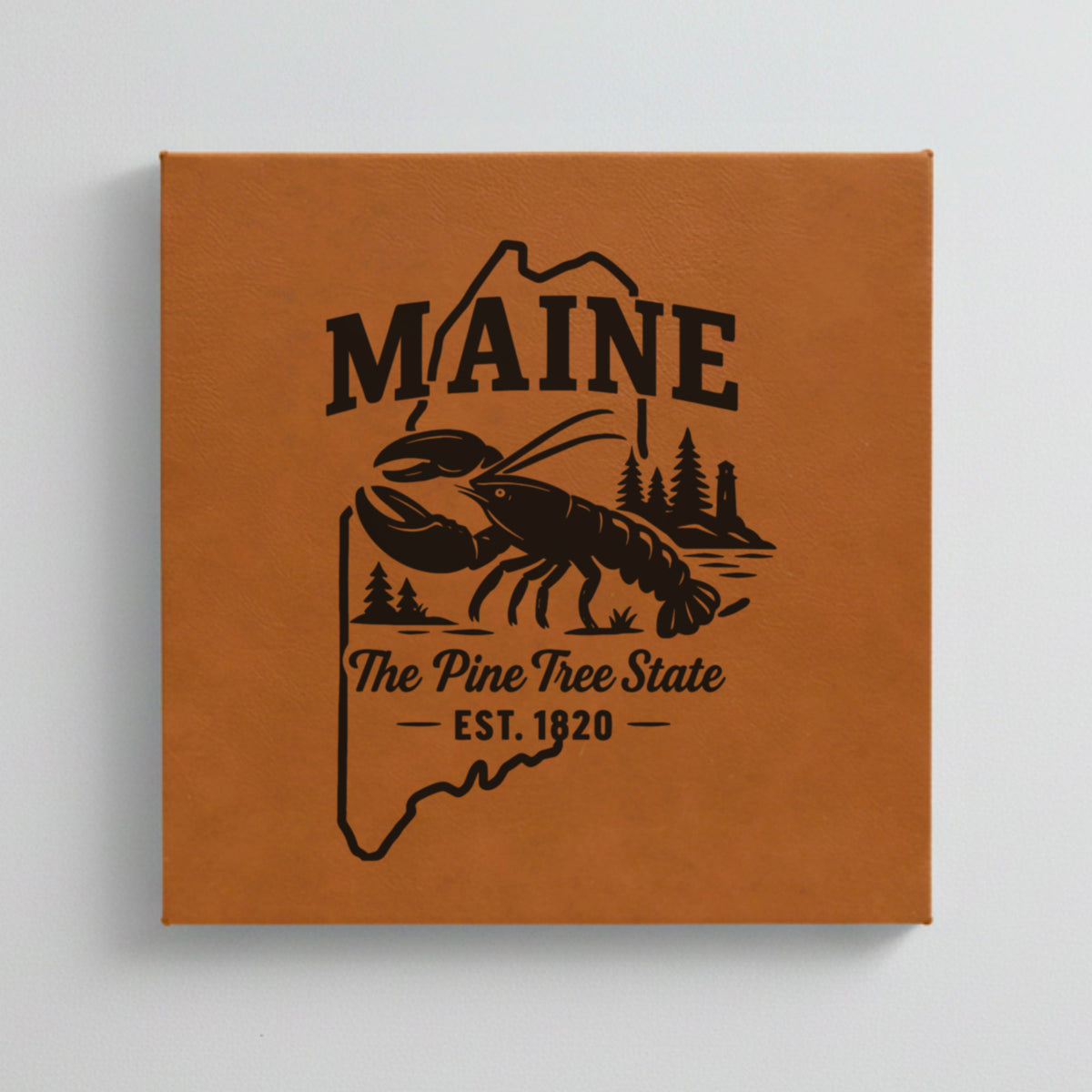 Close up of the Maine design engraved on Brown leatherette: a lobster, pines and a lighthouse, "The Pine Tree State", EST. 1820