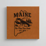 Close up of the Maine design engraved on Brown leatherette: a lobster, pines and a lighthouse, "The Pine Tree State", EST. 1820