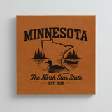 Close up of the Minnesota design engraved on Brown leatherette: a loon, a canoe and lakeside pines, "The North Star State", EST. 1858