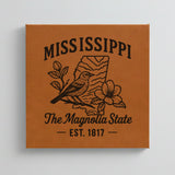 Close up of the Mississippi design engraved on Brown leatherette: a mockingbird and magnolia blossoms, "The Magnolia State", EST. 1817