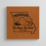 Close up of the Missouri design engraved on Brown leatherette: the Gateway Arch, a riverboat and a mule, "The Show-Me State", EST. 1821