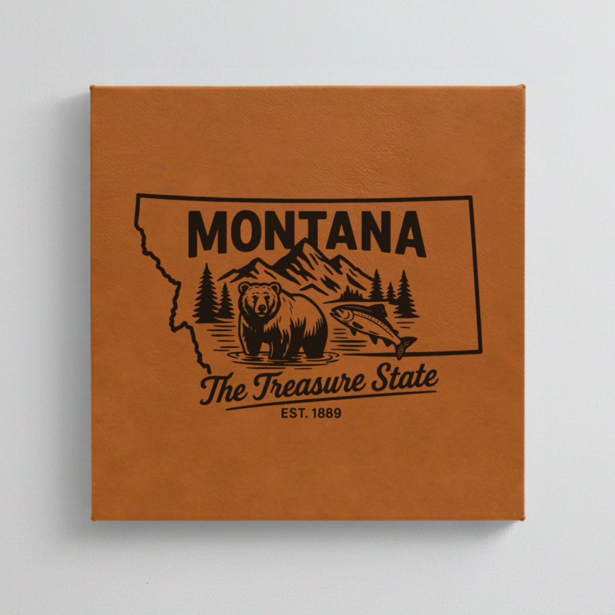 Close up of the Montana design engraved on Brown leatherette: a grizzly bear, a trout and mountain peaks, "The Treasure State", EST. 1889