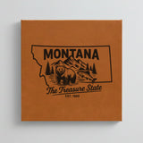Close up of the Montana design engraved on Brown leatherette: a grizzly bear, a trout and mountain peaks, "The Treasure State", EST. 1889