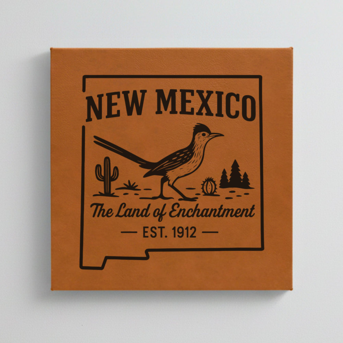 Close up of the New Mexico design engraved on Brown leatherette: a roadrunner, cactus and pines, "The Land of Enchantment", EST. 1912
