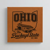 Close up of the Ohio design engraved on Brown leatherette: a covered bridge and a cardinal, "The Buckeye State", EST. 1803