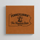 Close up of the Pennsylvania design engraved on Brown leatherette: the Liberty Bell, "The Keystone State", EST. 1787