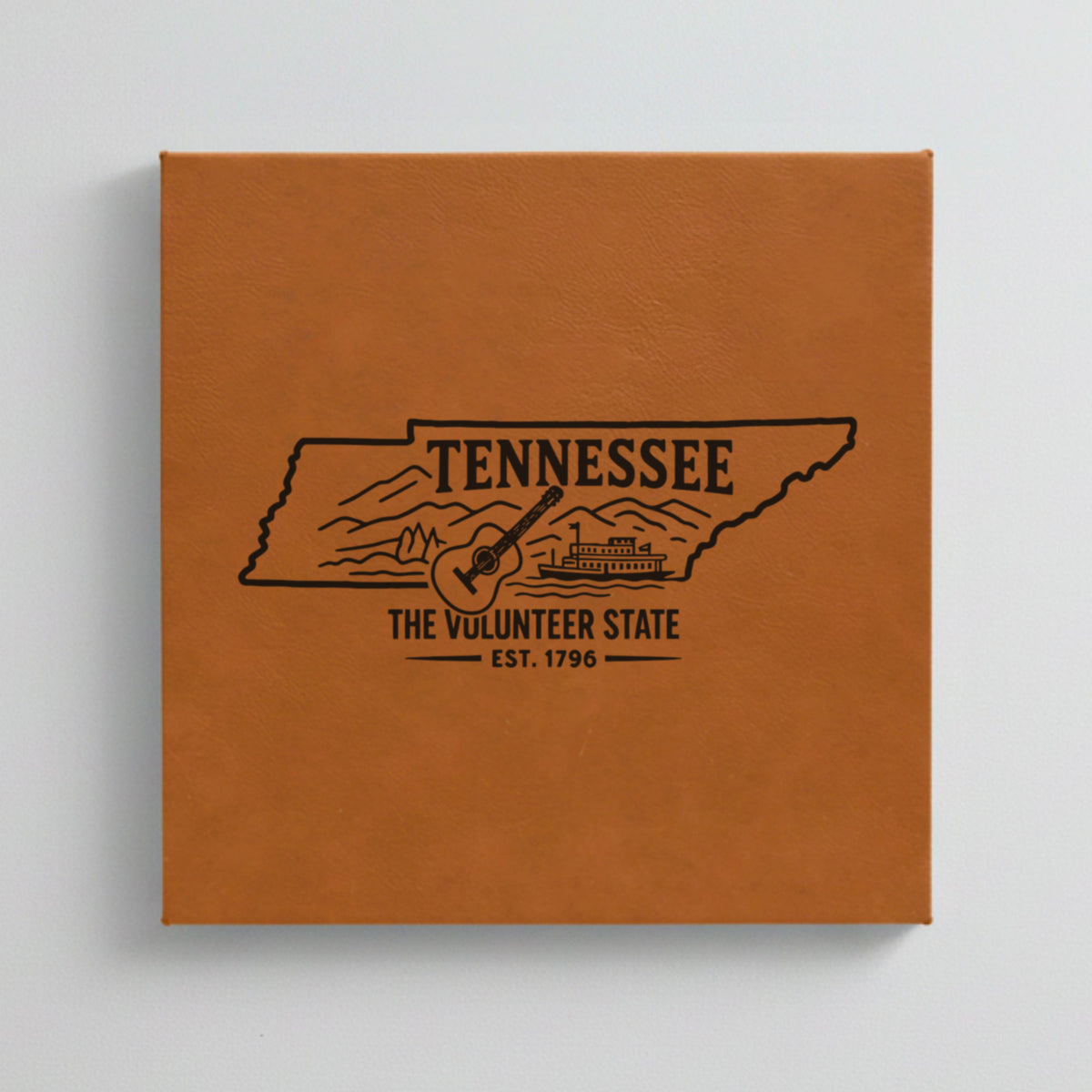 Close up of the Tennessee design engraved on Brown leatherette: a guitar, a riverboat and the Smoky Mountains, "The Volunteer State", EST. 1796