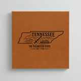 Close up of the Tennessee design engraved on Brown leatherette: a guitar, a riverboat and the Smoky Mountains, "The Volunteer State", EST. 1796
