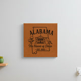 Brown leatherette wall sign engraved with an Alabama design of the capitol building, a cotton boll and a yellowhammer, hanging on a wall