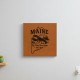 Brown leatherette wall sign engraved with a Maine design of a lobster, pines and a lighthouse, hanging on a wall